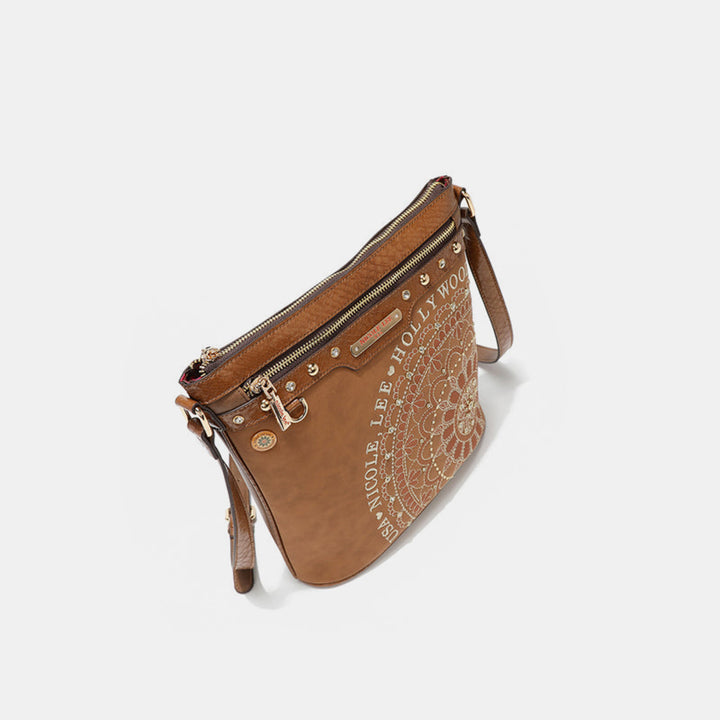The Nicole Lee USA crossbody bag features a brown vegan leather design with a detailed mandala pattern, decorative text, diamond rhinestones, zipper closure, metal studs, an adjustable strap, and a plain white background.