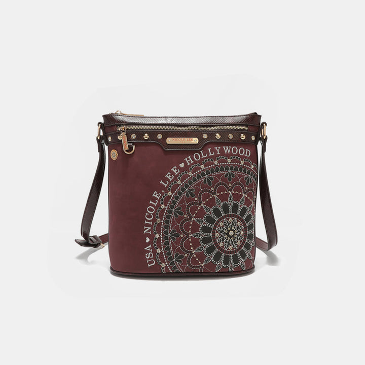 A chic maroon Nicole Lee USA crossbody bag with a circular mandala pattern, rhinestone details, made from vegan leather. It features a zippered top, adjustable strap, and Nicole Lee USA Hollywood text on the side.