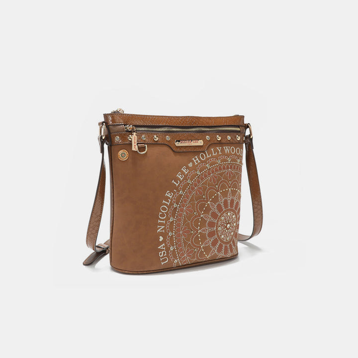 A crossbody bag by Nicole Lee USA made of brown vegan leather features intricate mandalas, USA Nicole Lee Hollywood text, a zippered front pocket, diamond rhinestones, decorative studs, and an adjustable strap.