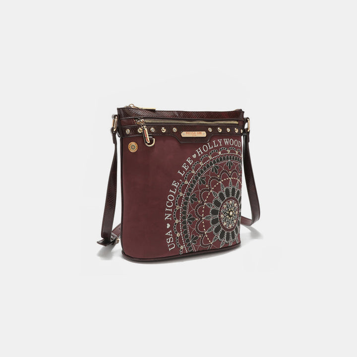 The Nicole Lee USA crossbody bag is crafted from vegan leather in maroon, featuring a detailed circular mandala pattern with gold studs and metallic stitching. It includes a zipper pocket and is adorned with USA Nicole Lee Hollywood encircling the design.