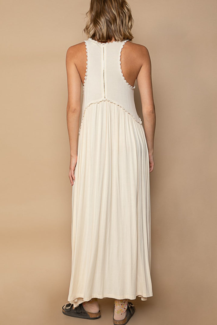 The person is seen from the back wearing a POL Sleeveless Back Zipper Front Slit Maxi Dress, showcasing its racerback and babydoll silhouette. This cream knit dress flows gracefully with a loose fit against a beige background. They pair it with dark sandals on a light surface.