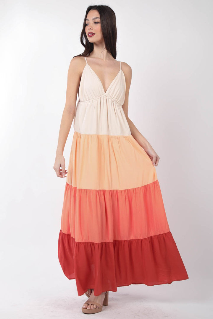 A woman models the VERY J Color Block Tiered Maxi Cami Dress with elegance, showcasing its flowy design and beautiful cream, peach, pink, and red tiers against a plain white background.