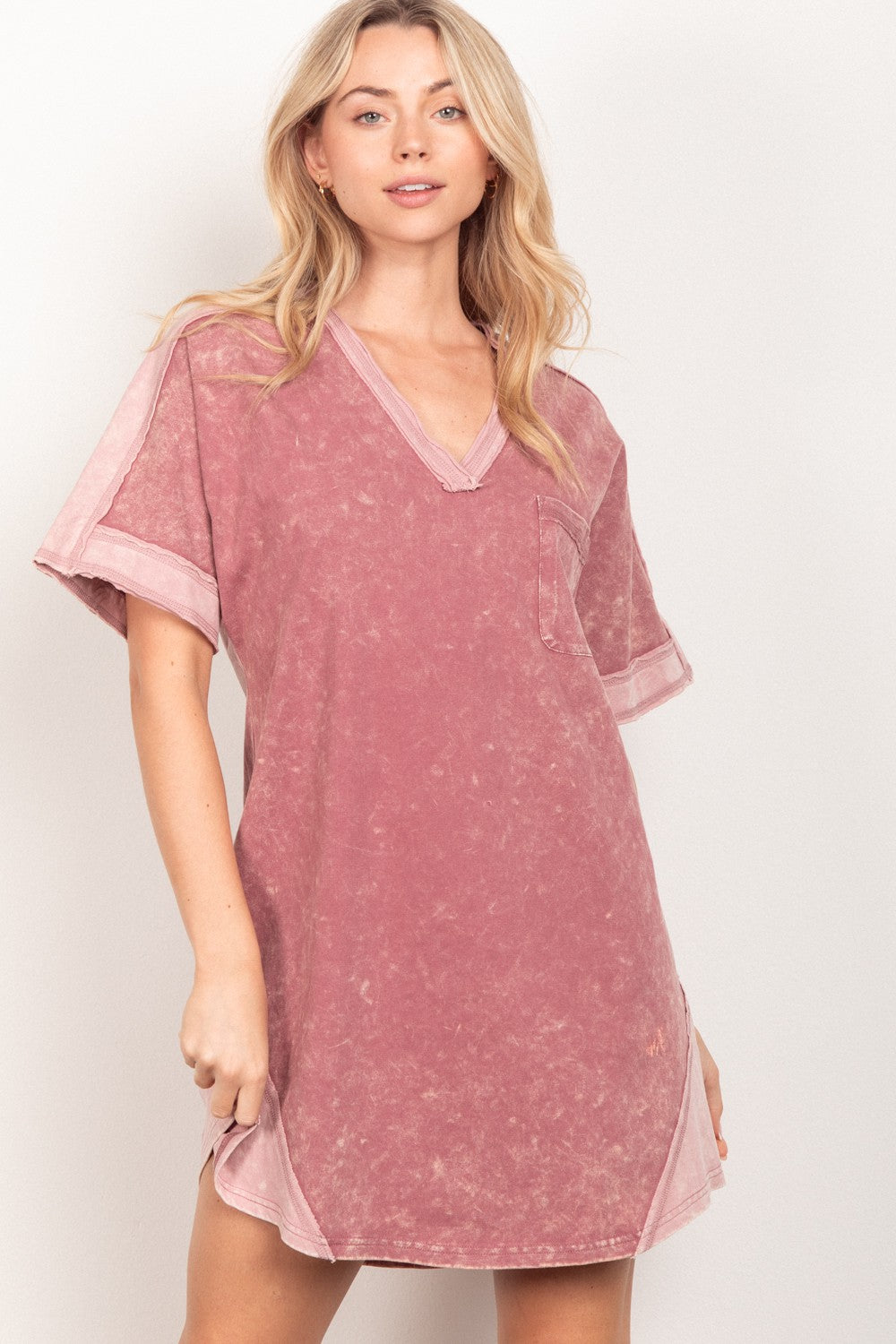 A woman models the VERY J Short Sleeve V-Neck Tee Dress, featuring a chest pocket and side slits, standing confidently against a plain light background.