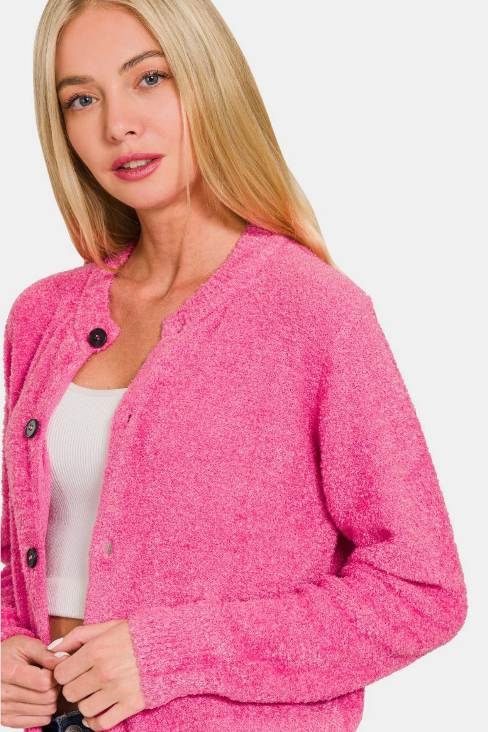 A woman with long blonde hair is wearing a bright pink Zenana Button Down Long Sleeve Sweater Cardigan over a white top. She is looking towards the camera with a neutral expression against a plain white background.
