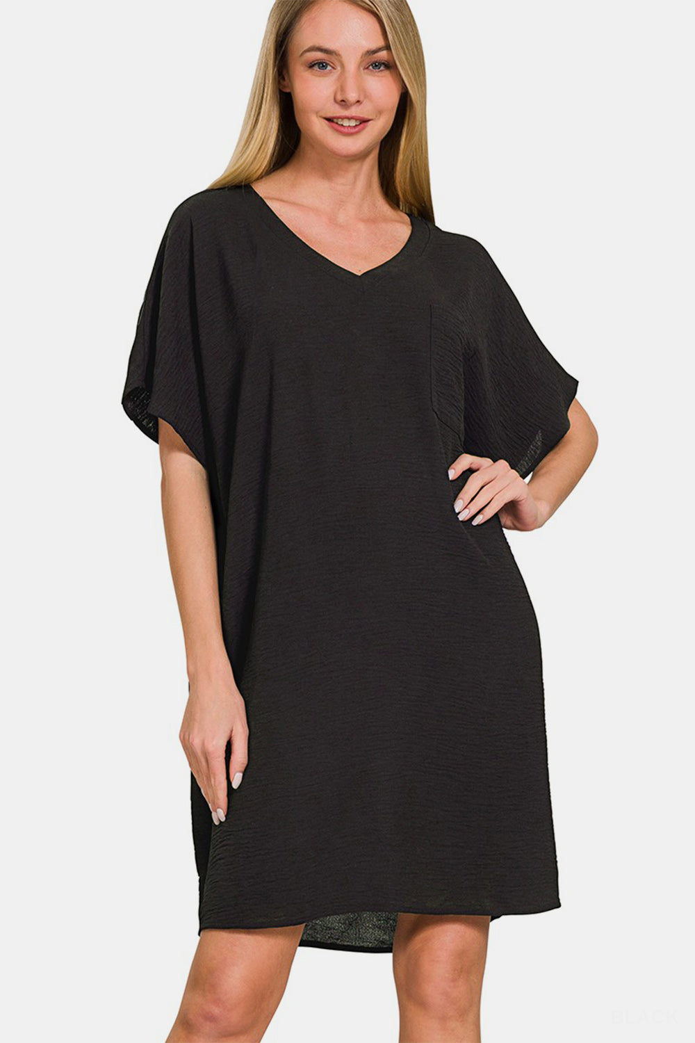 A woman stands with one hand on her hip, smiling in the Zenana V-Neck Tee Dress with Pockets—a versatile, loose-fitting short sleeve dress.