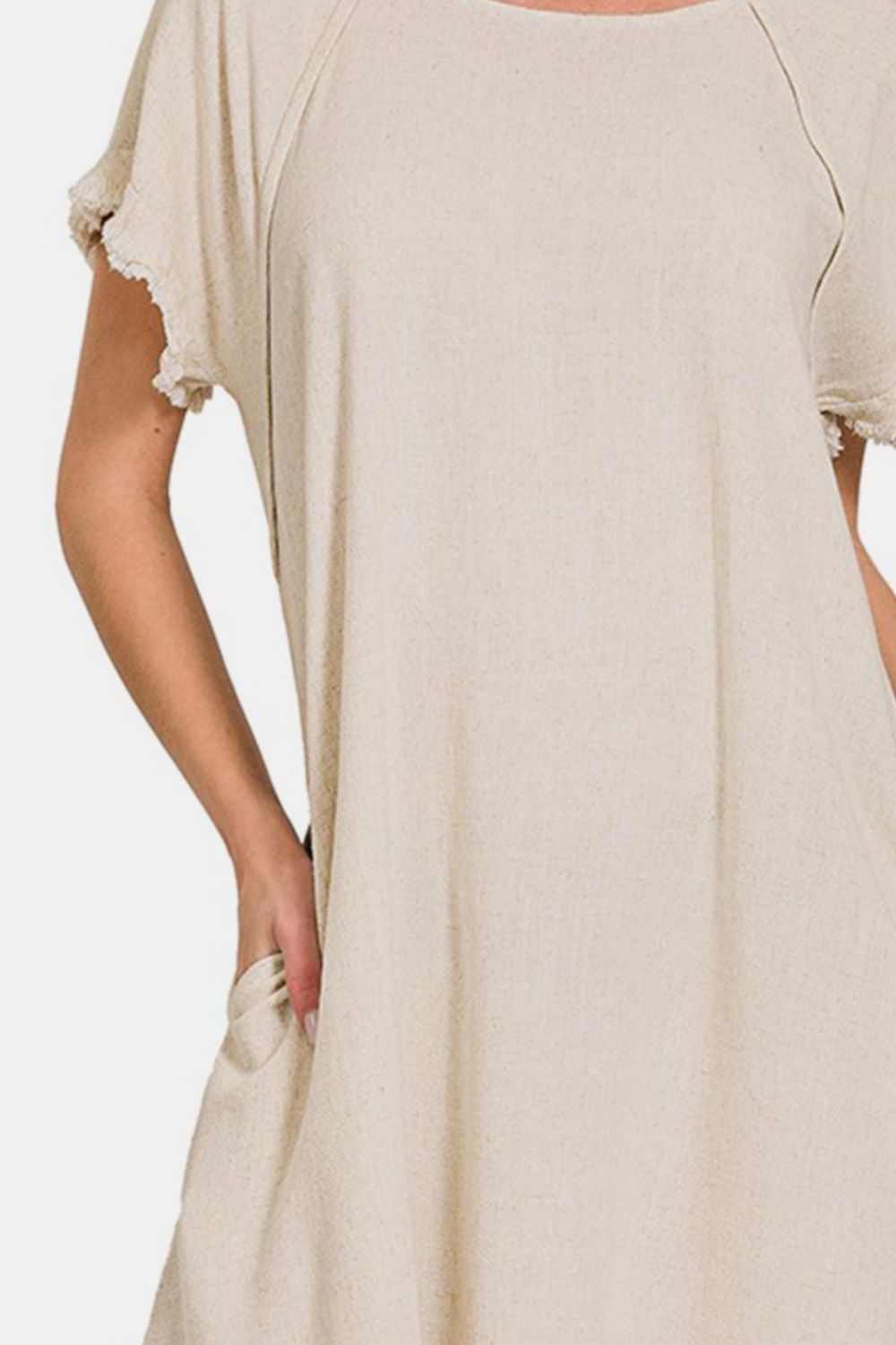 A person is wearing the Zenana Fringe Edge High Low Flowy Dress with Pockets, a beige dress featuring short sleeves, frayed edges, and a high-low design. The background is plain white.