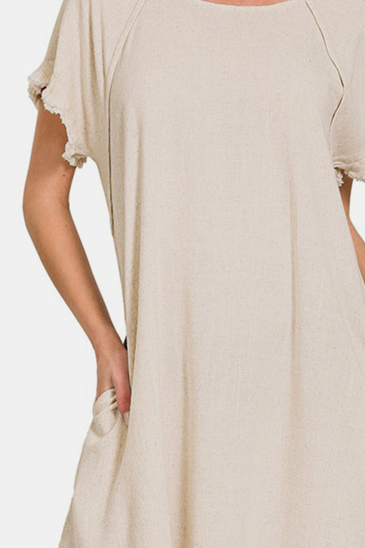 A person is wearing the Zenana Fringe Edge High Low Flowy Dress with Pockets, a beige dress featuring short sleeves, frayed edges, and a high-low design. The background is plain white.